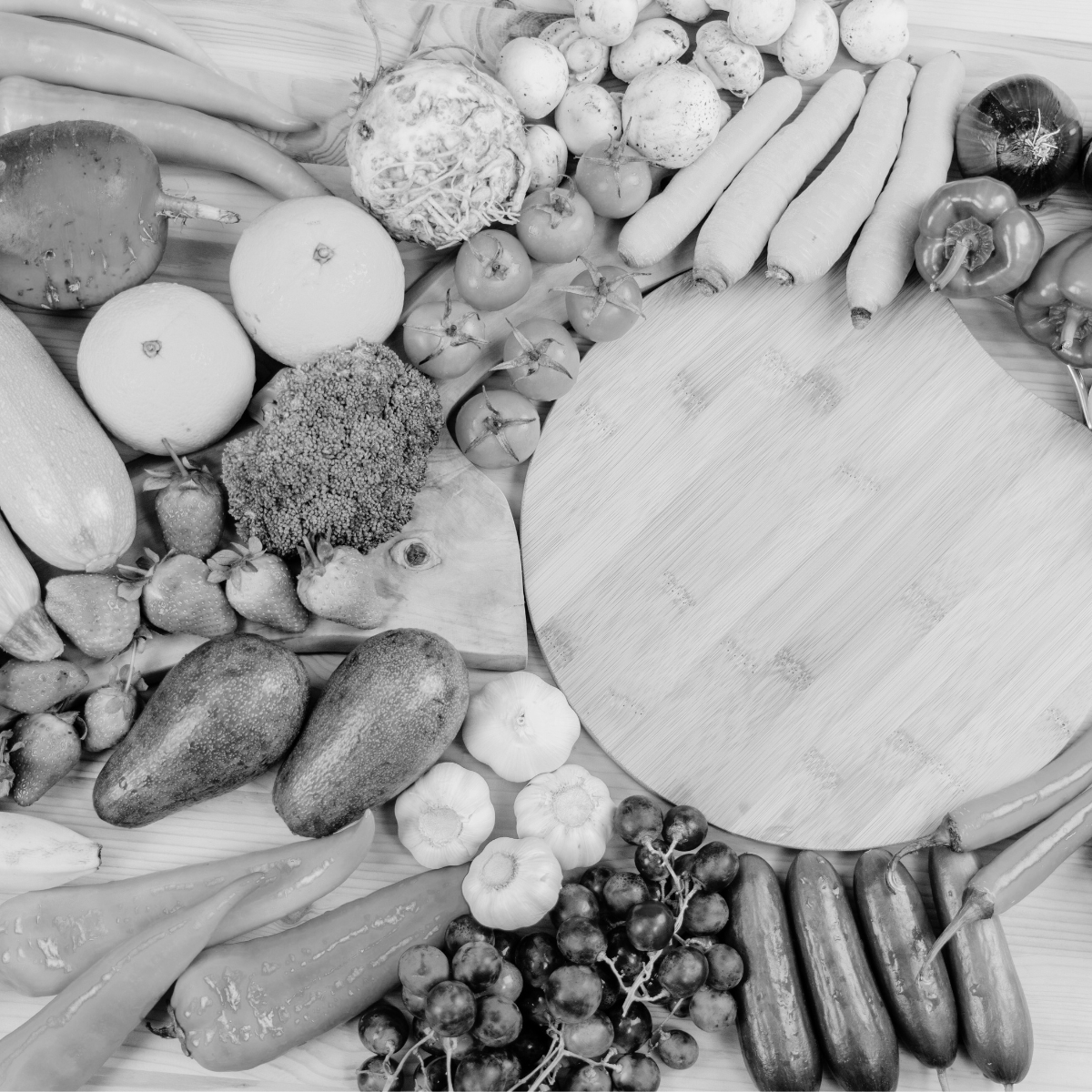 Black and white image of a wooden cutting board surrounded by various fruits and vegetables.